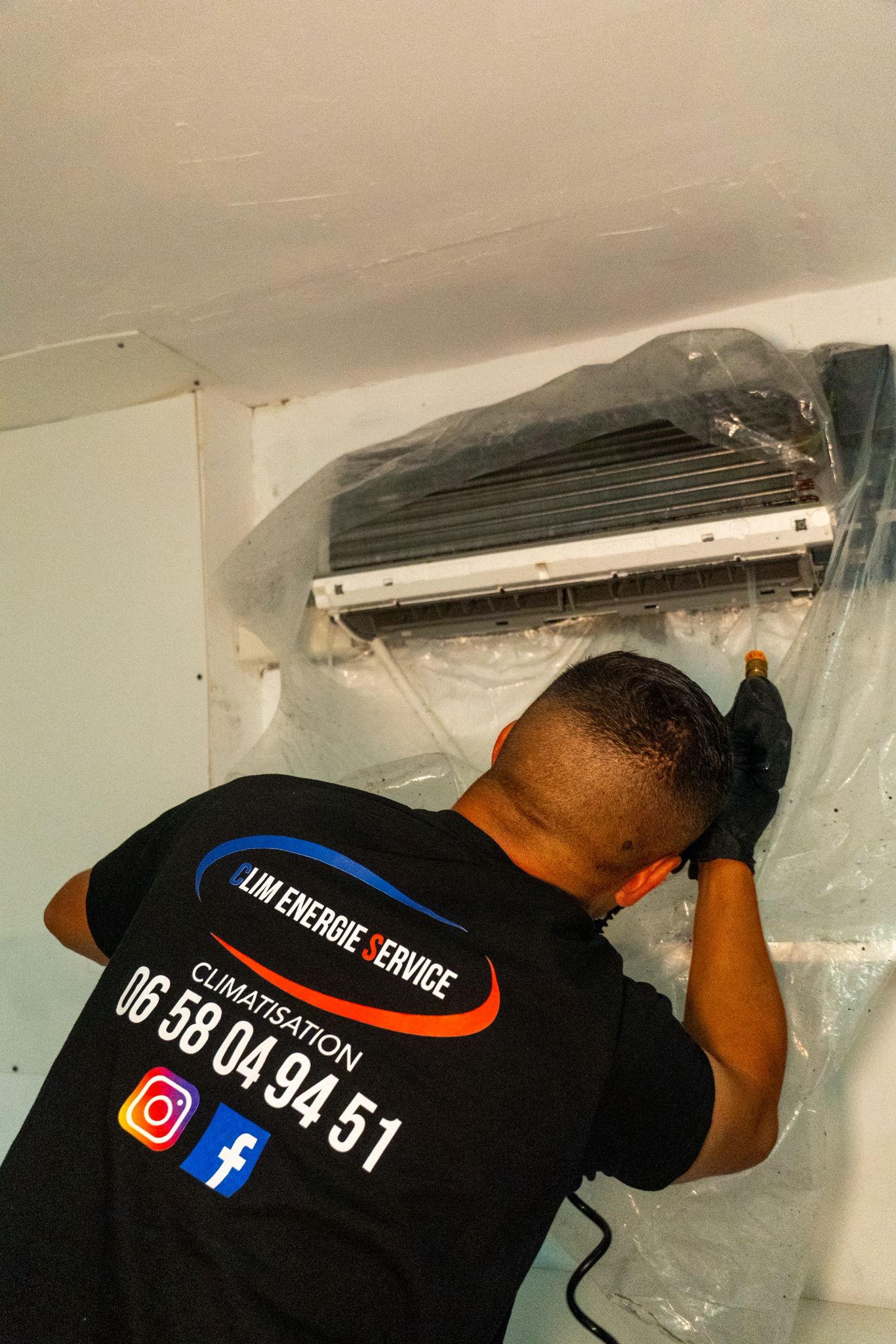 Technicien Clim Energie Service nettoyant une climatisation murale avec une bâche de protection